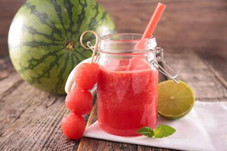 a cup of juice with a straw in it, surrounded by watermelon