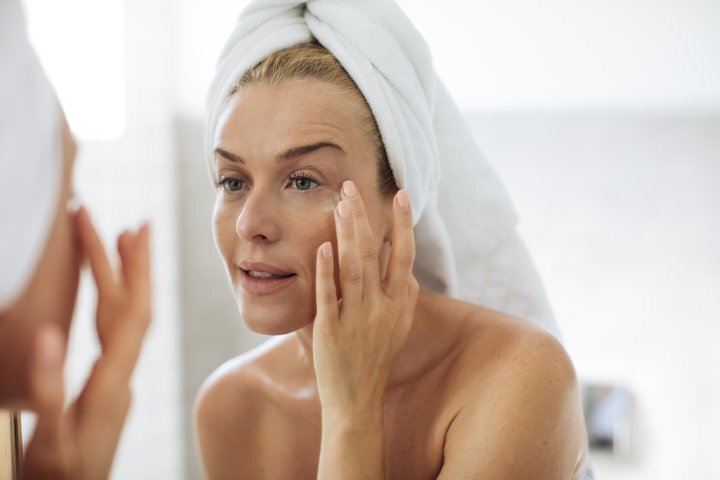 a woman looking at her skin in the mirror after a shower