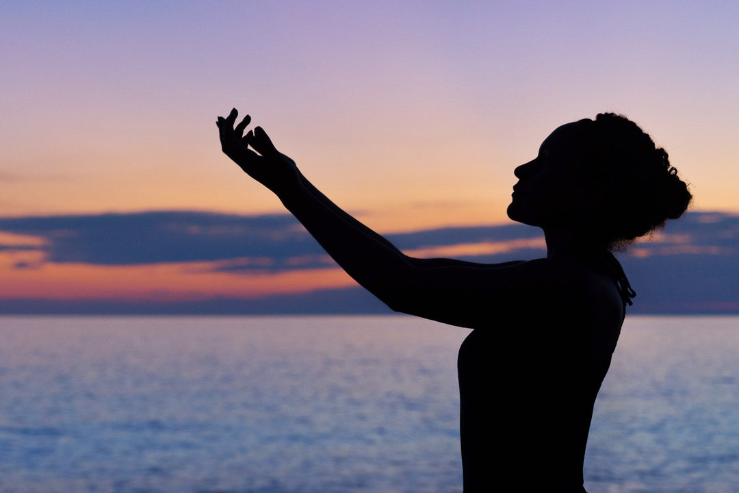 a silhouette of a young woman near the beach holding her arms up